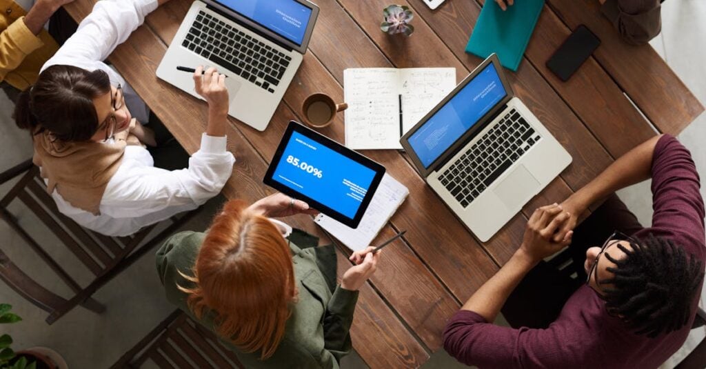 Diverse team discussing business strategies with laptops and tablets at a wooden table.